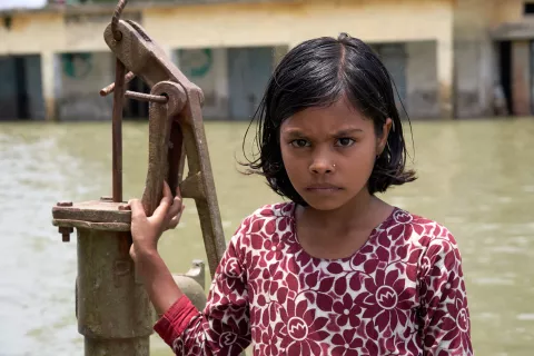 A girl stands in floodwater in front of a well, Bangladesh