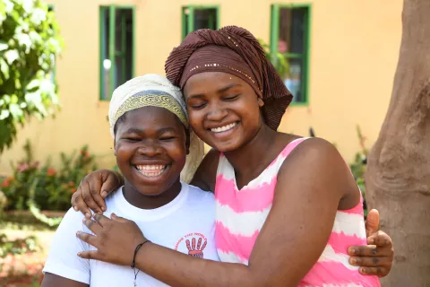 Aminata Sawadogo (right), 16, and Sandrine (left), 17, hugging each other and smiling in Burkina Faso.
