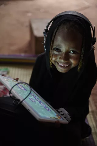 A girl child smiles while using her tablet and headphones in Eastern Sudan in 2019.