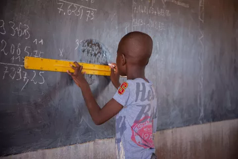 A child uses a rule to draw a line on a chalkboard.