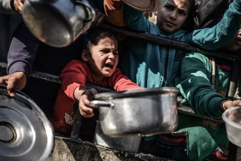 A girl stretches her arms out holding a metal pot in a food line in the Gaza Strip 
