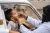 Une agente de santé portant une blouse blanche, donne des gouttes (vaccin) à un enfant à travers la fenêtre d'une voiture.