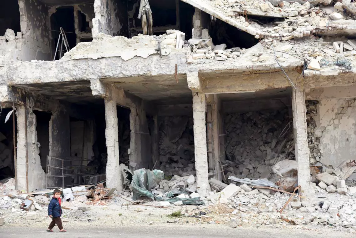 Un enfant marche devant des bâtiments en ruine 