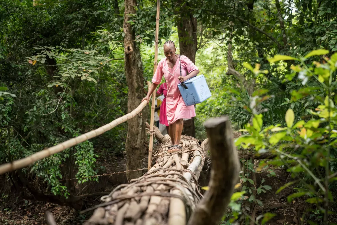 A nurse crosses a hand-made bridge carrying a vaccine cooler to reach the remote village of Mansunthu to conduct a mobile vaccination clinic.