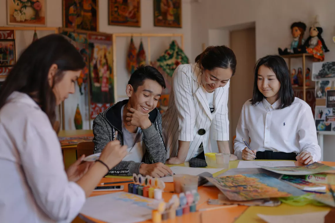 A group of young people laugh together at a table in art school as they draw and paint in Kazakhstan in 2019.