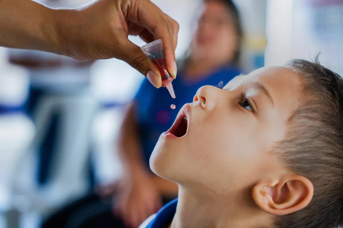 Un jeune garçon, la tête penchée en arrière et la bouche ouverte, attend que le vaccin contre la polio lui soit administré.