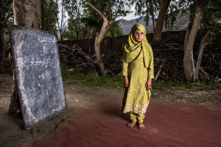 Una niña junto a una pila de escombros de metal de lo que fue una escuela en Afganistán