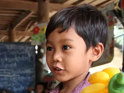 A boy in a classroom holds a banana bunch of plastic. 