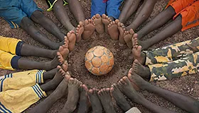 Circle of boys' bare feet with the soccer ball at a UNICEF Child-Friendly Space in Ouahigouya, Burkina Faso.