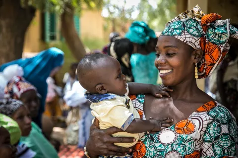 A smiling woman holds a baby in her arms.