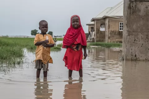 Two children standing amid their flooded village