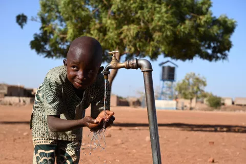 A young boy washing his hands using a tap in his community
