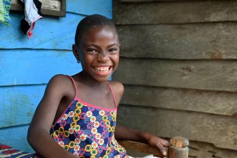A young girl with short hair smiling while sitting outside