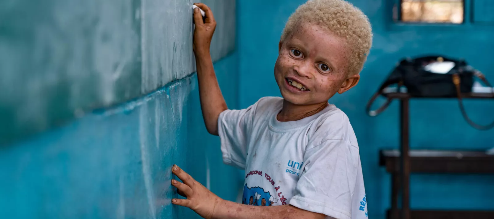 A child smiles as he writes on the blackboard in his classroom