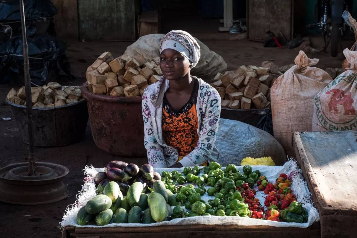 A woman sitting in a market with vegetables on the table